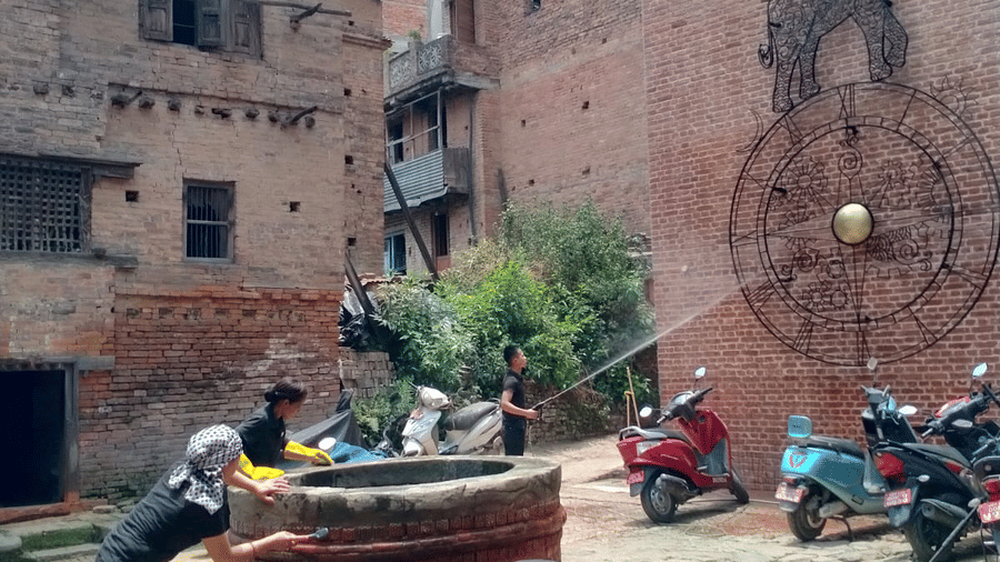 Vertical view of volunteers scrubbing a historic brick water well structure during a community cleanliness drive in Bhaktapur, Nepal.