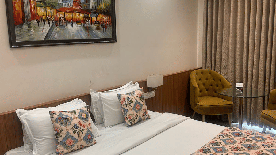 A Superior Room at the Prince ZENQ Xpress Resortt Rohtak, featuring a large bed with a floral runner, decorative pillows, a painting on the wall, and two velvet armchairs with a glass side table.