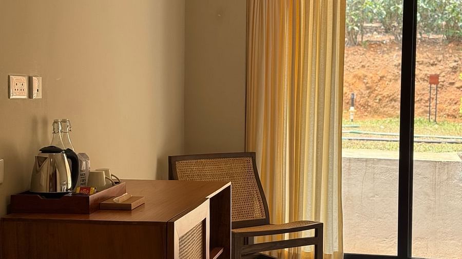  A hotel room interior featuring a wooden cabinet with a kettle, a chair, and a large sliding glass door leading to a balcony.