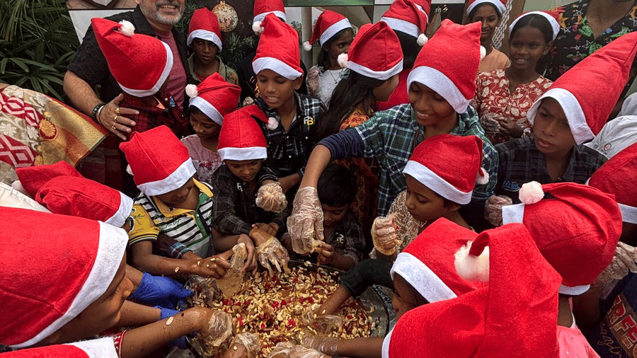 A large group of people wearing Santa hats gathered together at a Christmas celebration event at Vedic Village Spa Resort in a festive outdoor setting.