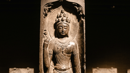 Ancient stone sculpture displayed inside a museum, lit softly to highlight carved details and historical features.