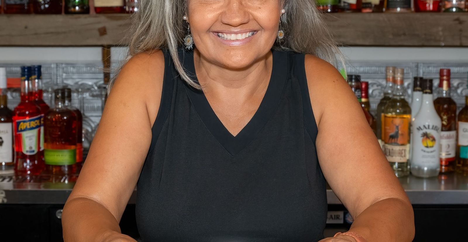 Smiling woman seated at the bar with a plated dessert in front of her at The Groveland Hotel.