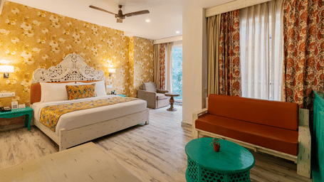 A well-lit suite featuring brightly coloured furniture, an accent wall, full length curtains, and an attached balcony | Summit by the Ganges Beach Resort & Spa, Rishikesh