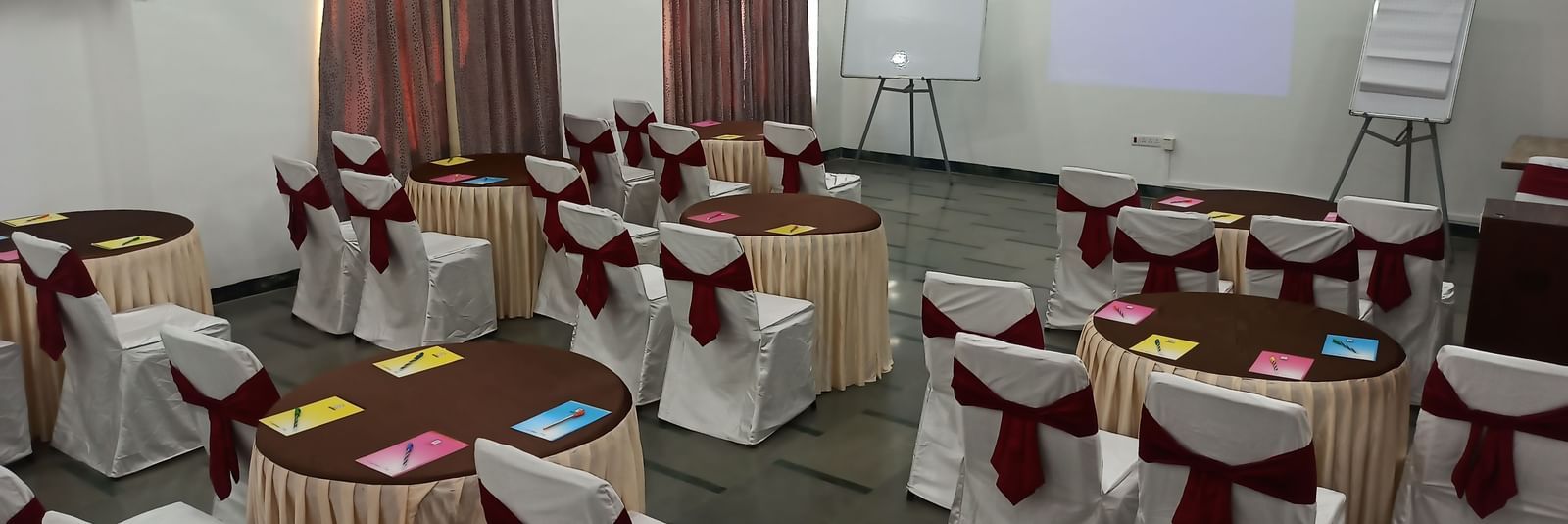 Training room setup with cluster seating arrangement, notepads, and a projection screen at Mayur Retreat.