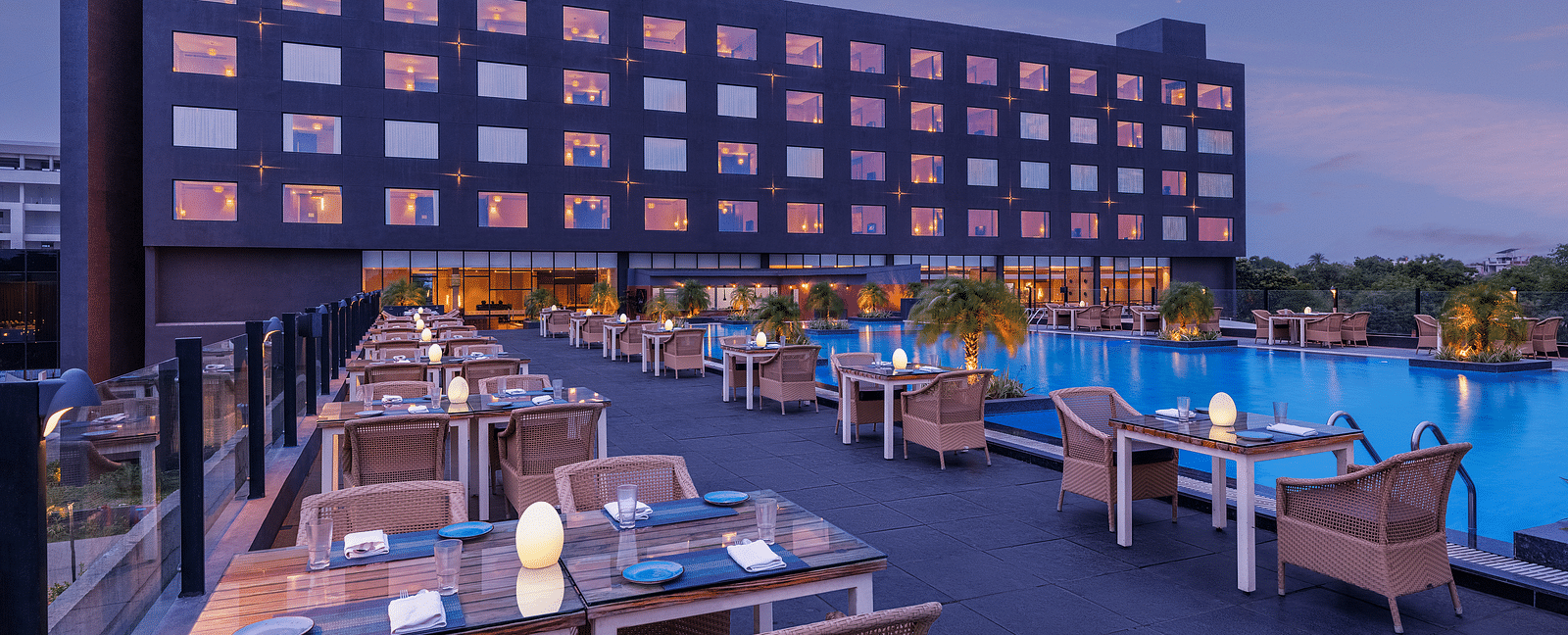 Poolside seating arrangement with the Essentia Luxury Hotel, Indore building in the backdrop