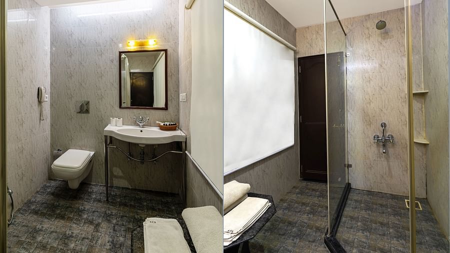 A spacious bathroom featuring a wall-mounted mirror above the washbasin, a western toilet adjacent, and a glass partition that separates the shower area | Panna Vilas Udaipur