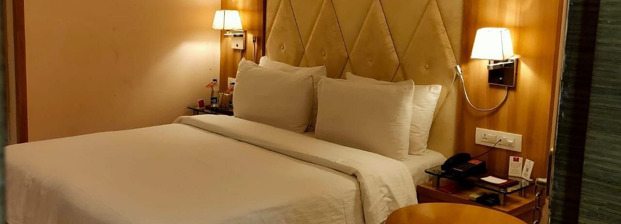 A cosy hotel bedroom  featuring a neatly made bed, bedside lamps, and a decorative headboard - Rang Lords Inn Bharuch