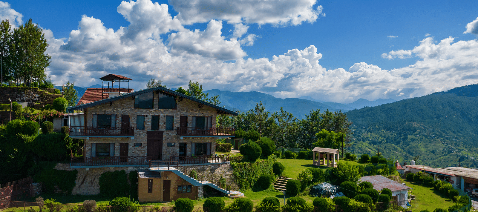 A charming villa surrounded by lush greenery and set against the backdrop of rolling hills and blue skies. - Blusalzz Homes The Himalayan Bungalow, Almora