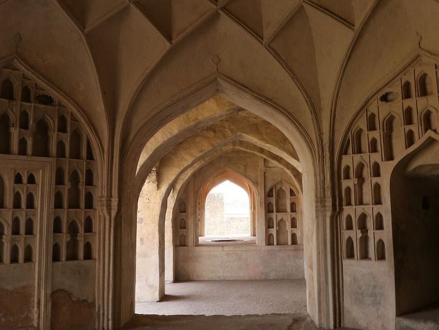 A dimly lit corridor with arched doorways and intricate latticework. The walls are adorned with intricate carvings and designs.