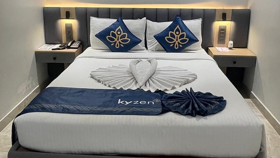Bed with decorative cushions, side tables, and soft lighting, featuring towel art in the shape of a heart at Hotel Kyzen HiTech City – Your Zenly Stay