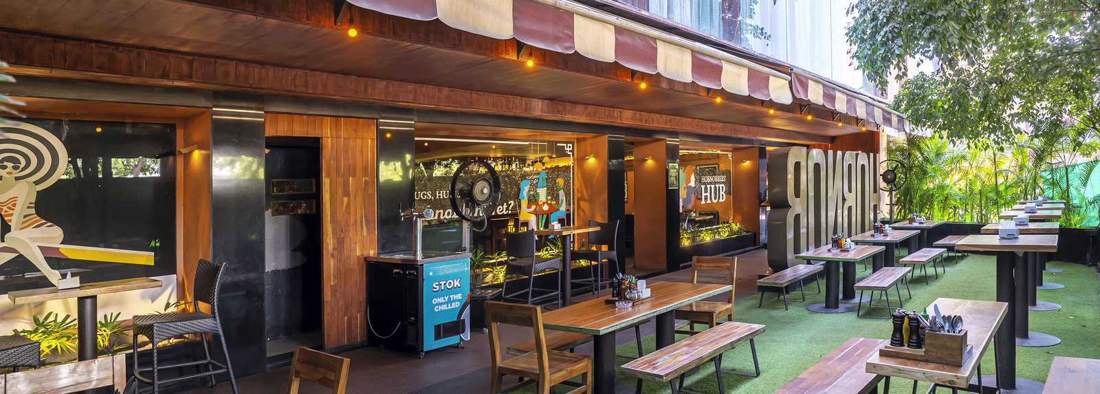 An outdoor seating area with tables, chairs and a long building wall decorated with signs at Infiniti Hotel, Indore.
