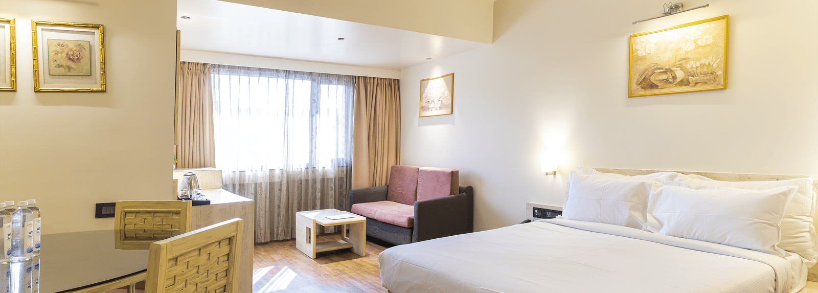 Bedroom with a king size bed, dining table & chairs, a seating space by the window and painting on the wall at Infiniti Hotel, Indore.