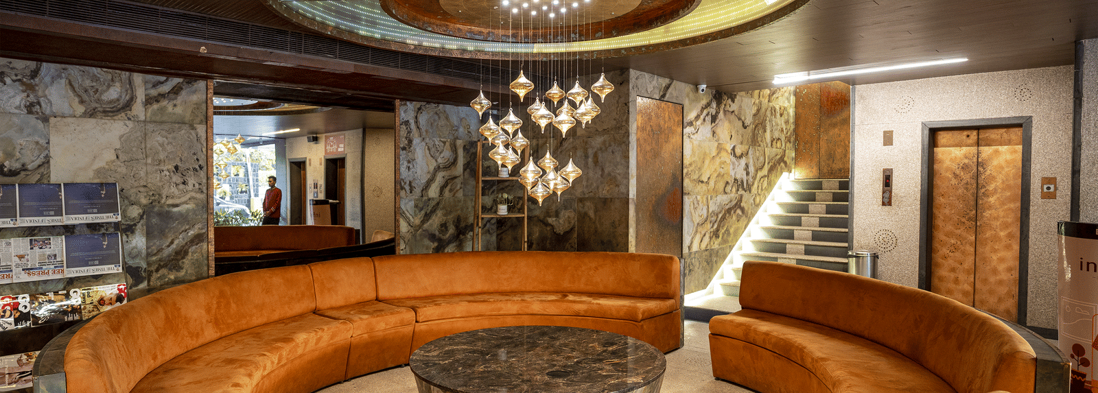 Interior of a lobby with circular wooden seating, a modern chandelier, and polished stone surroundings at Infiniti Hotel, Indore.