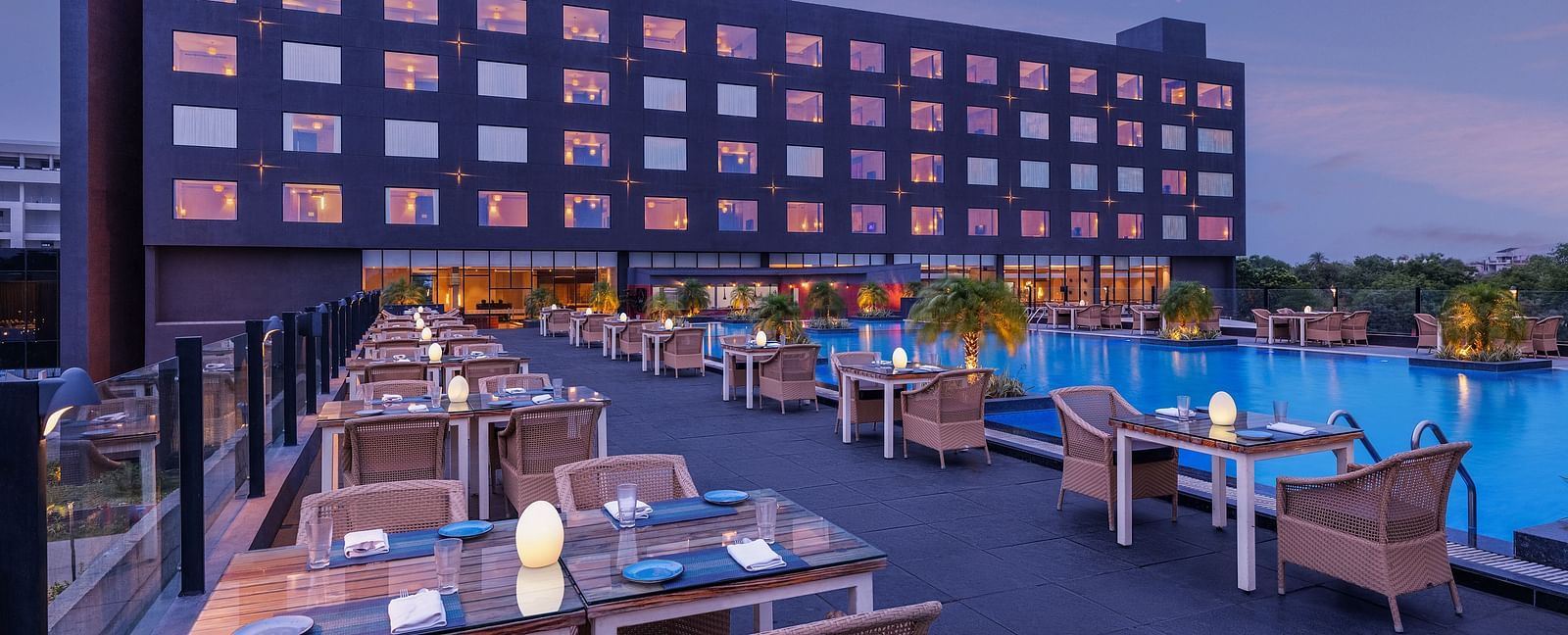 Poolside seating arrangement with the Essentia Luxury Hotel, Indore building in the backdrop