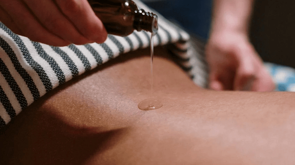 A massage therapist poruing oil on the back of  a person in a spa.