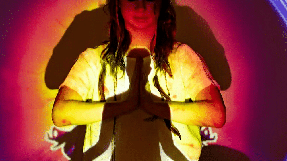 A woman meditating with her eyes closed and colourful halo projected over her.
