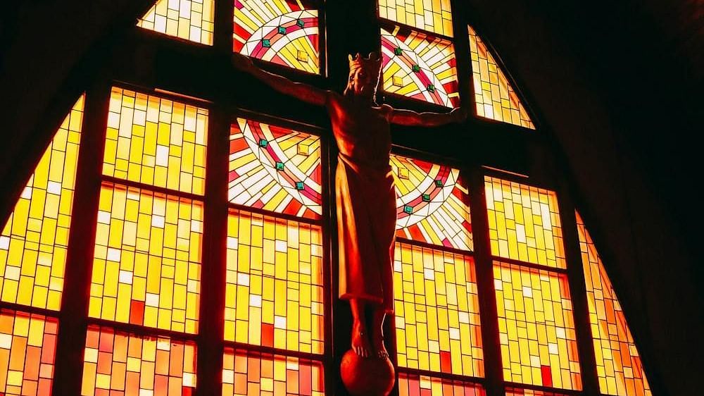 An image of Jesus on the crucifix set against the backdrop of stained glass windows.