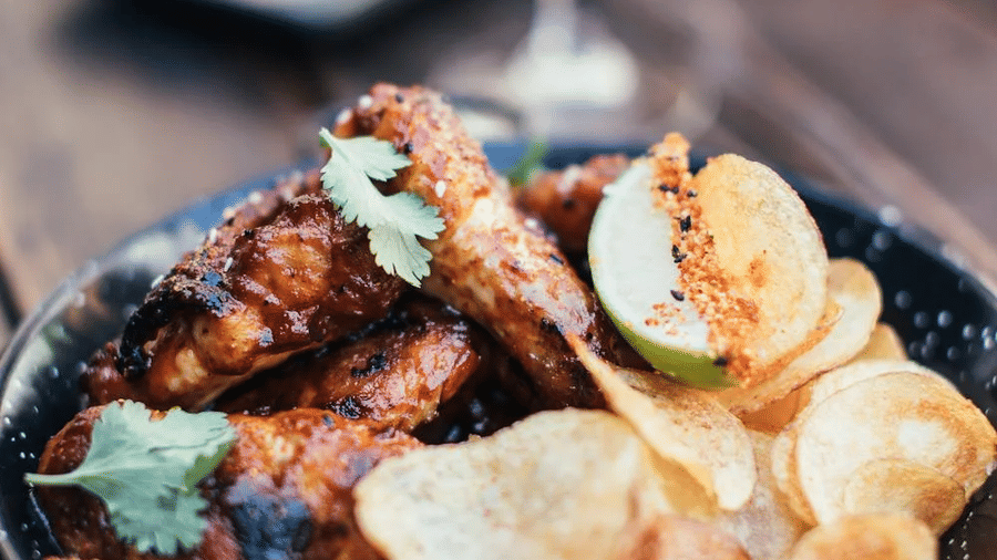 A close-up of crispy chicken wings with chips and a refreshing drink, available at the Tallman Hotel.