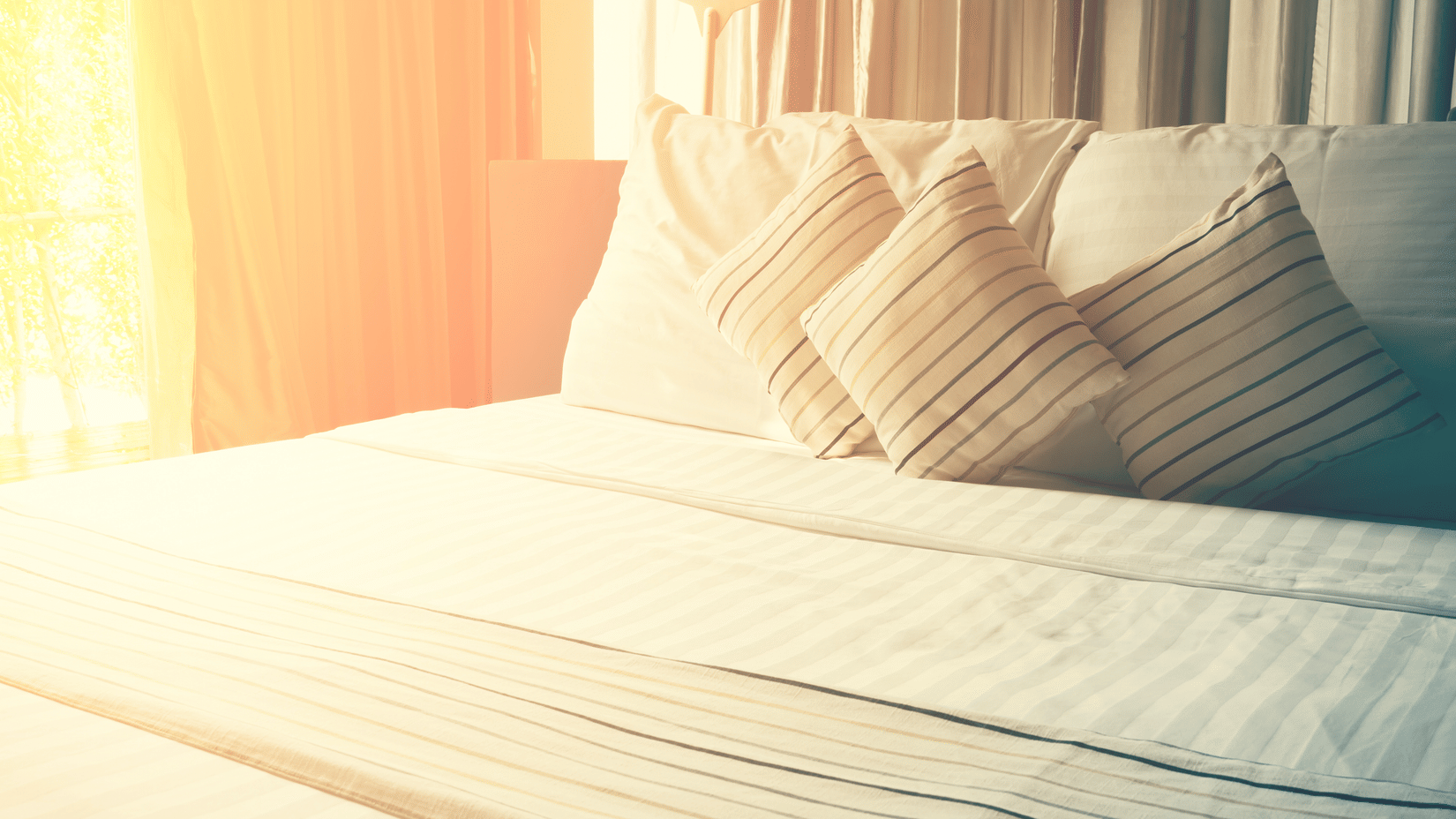 A sunlit bedroom with neatly made bed and pillows 