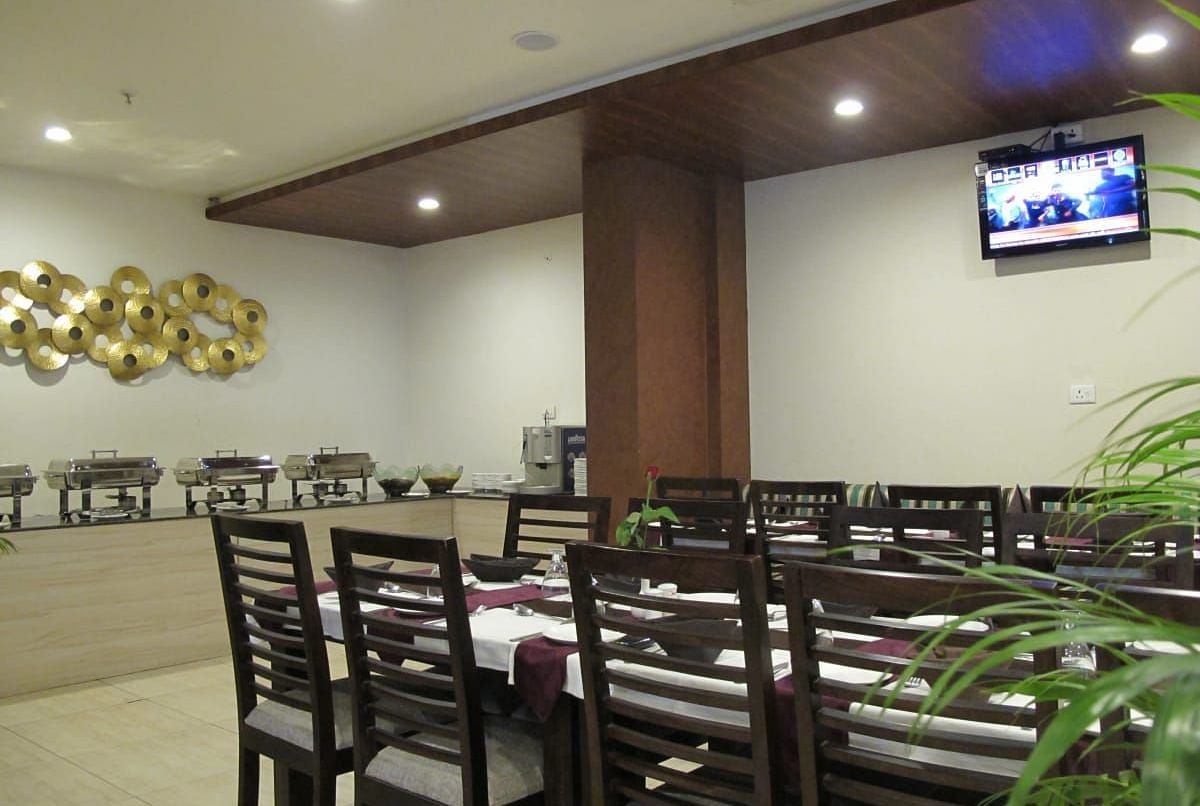 A spacious dining area with a buffet setup, wooden furnishings and a television mounted on the wall - TGI Apple Inn, Jaipur 