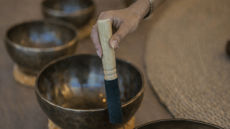 A person stirring a metal vessel to create a vibrating sound for healing.