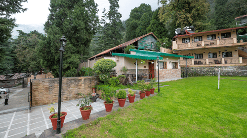 Garden area at The Pavilion, Nainital showing terracotta planters, manicured lawn, stone pathways, and traditional hill station architecture.