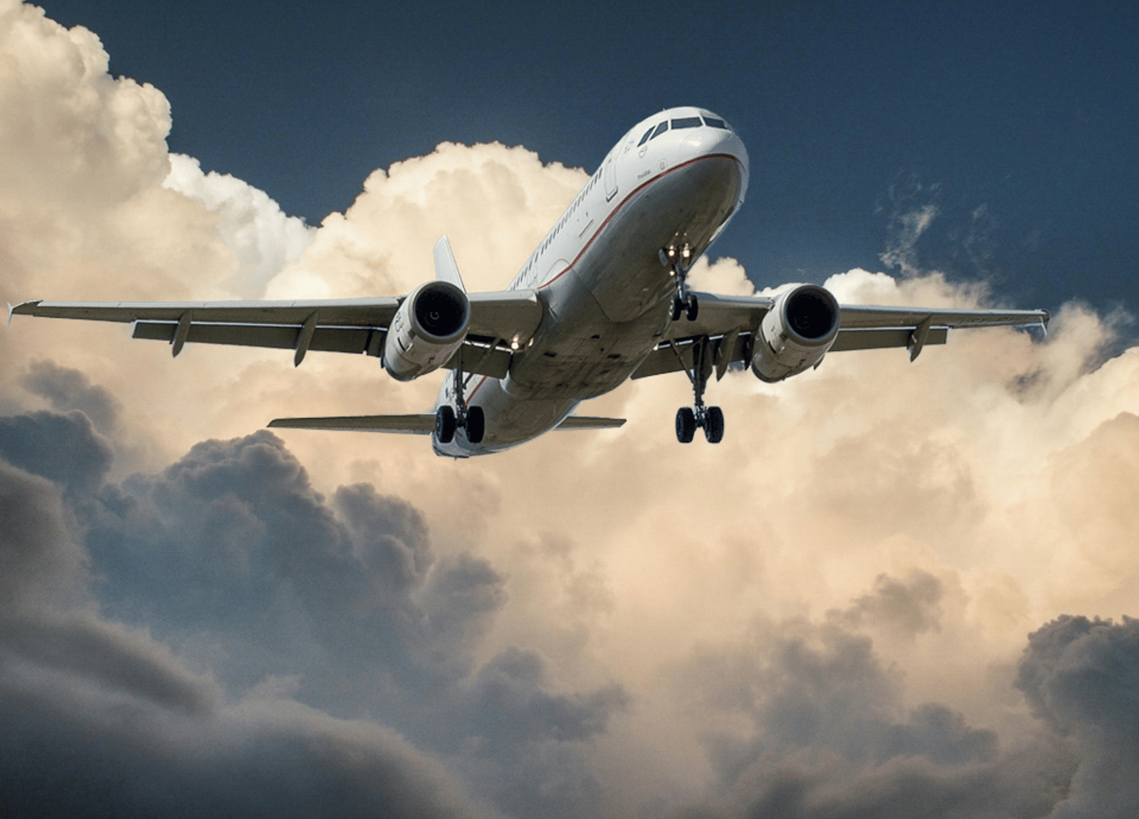 An aircraft soaring through the sky with clouds in the background.