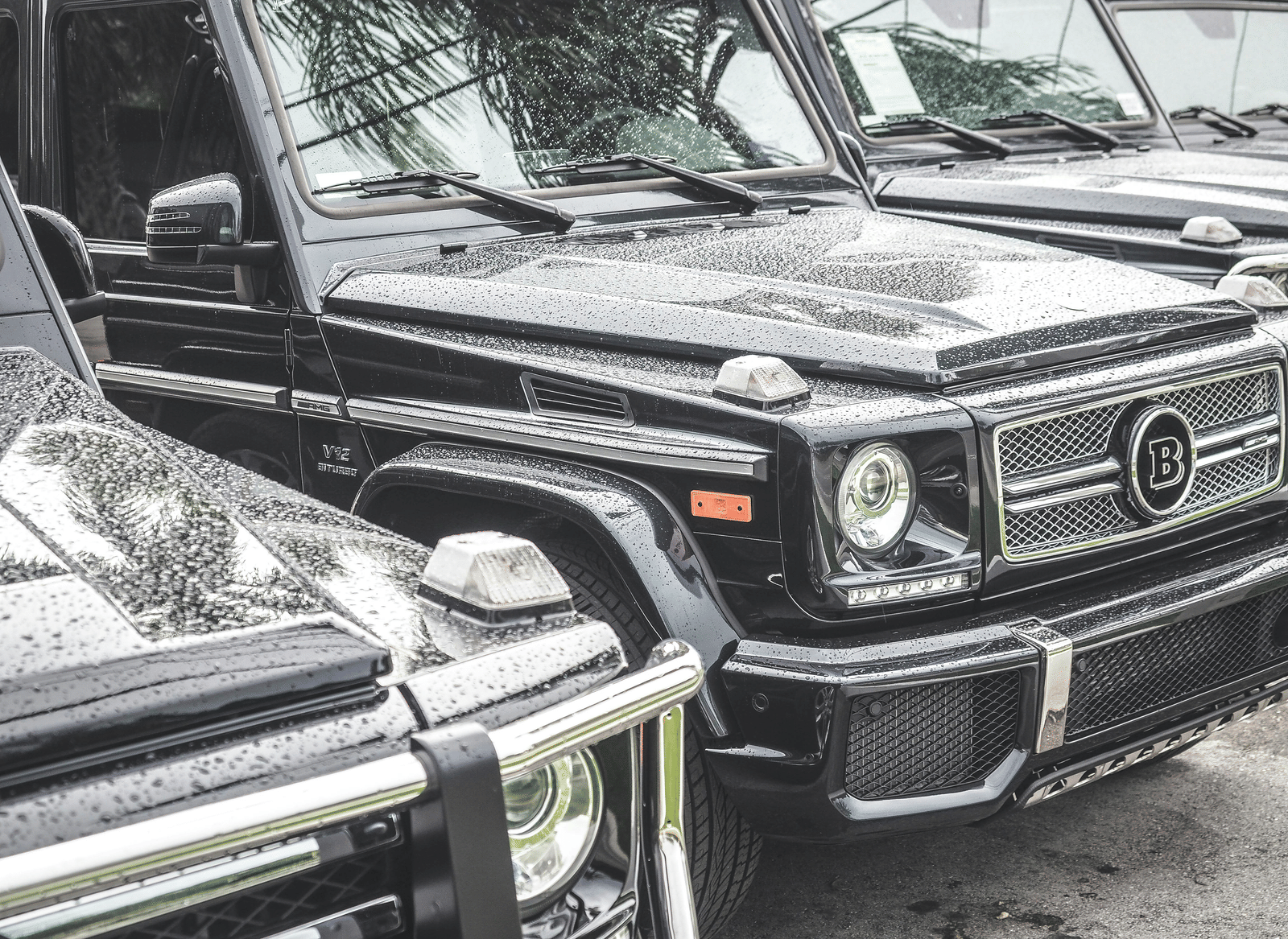 A row of large, boxy 4-wheel drive vehicles parked closely together, with rain visible on the bodywork.
