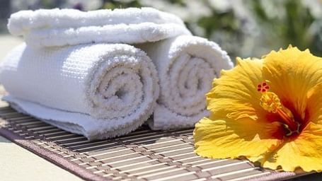 A yellow hibiscus flower on top of a table placed alongside freshly folded white towels.
