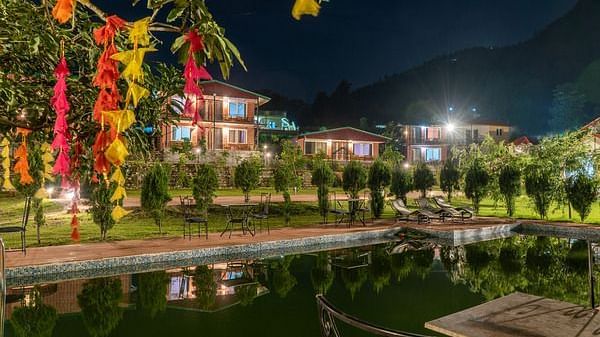 overview of the swimming pool with plants covering the outside at night - Neer Ganga Resorts