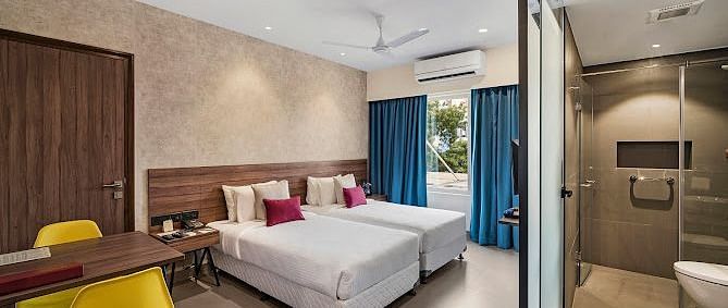 One of our rooms in thoothukudi with twin beds, a table with yellow chairs, and a modern shower area in front - Regency Tuticorin by GRT Hotels