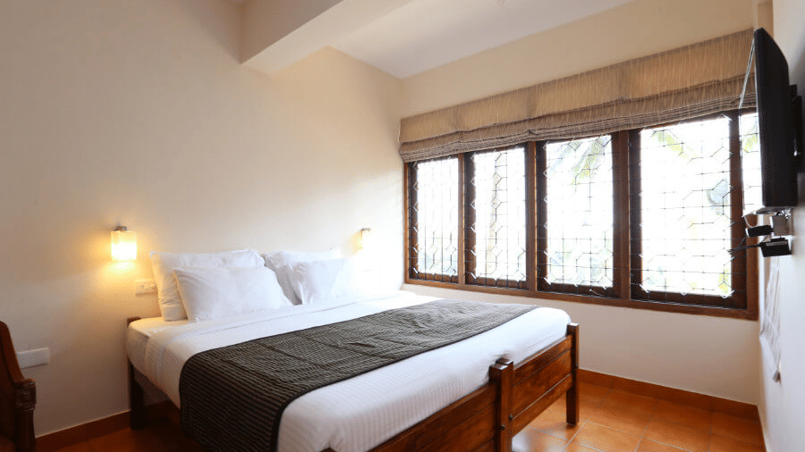 The deluxe room bedroom at Abad Serviced Villas, Kovalam with a double bed, bedside table, lamp, and large windows.