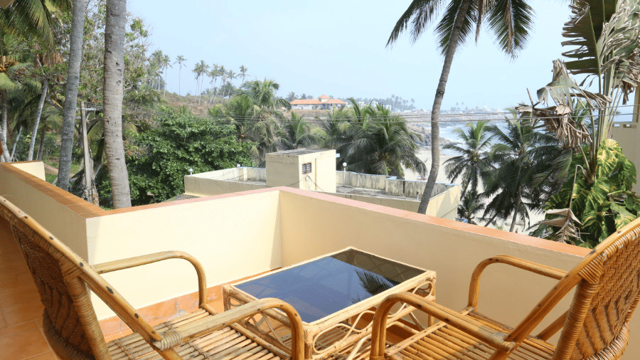 A private balcony of a deluxe room at Abad Serviced Villas, Kovalam with chairs, a table, and a view of trees and the sea.