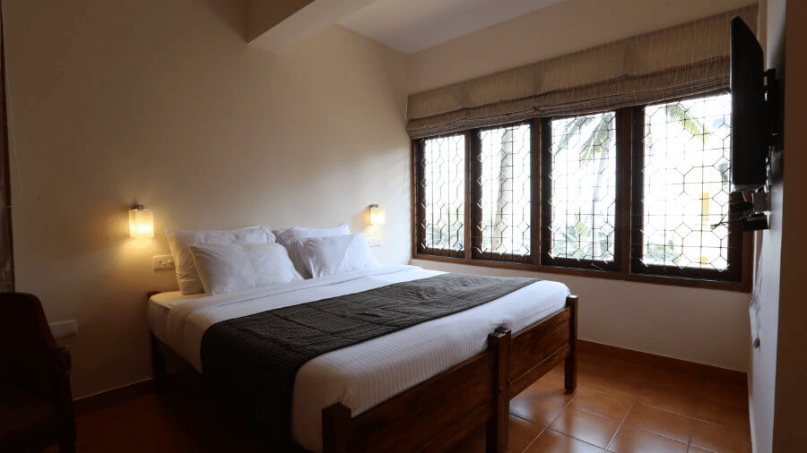 A deluxe room bedroom at Abad Serviced Villas, Kovalam with a double bed, bedside table, lamp, and large windows.