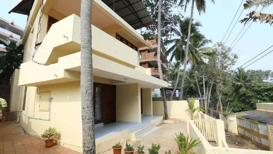 The Facade of Abad Serviced Villas with balconies, a tiled pathway, and surrounding trees.