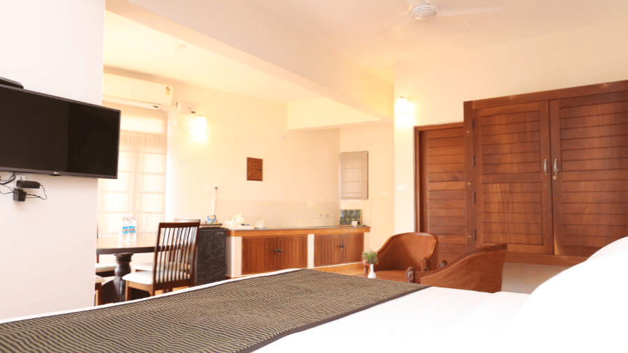 A superior room at Abad Serviced Villas, Kovalam showing a bed, wall-mounted television, seating area, and wooden furniture