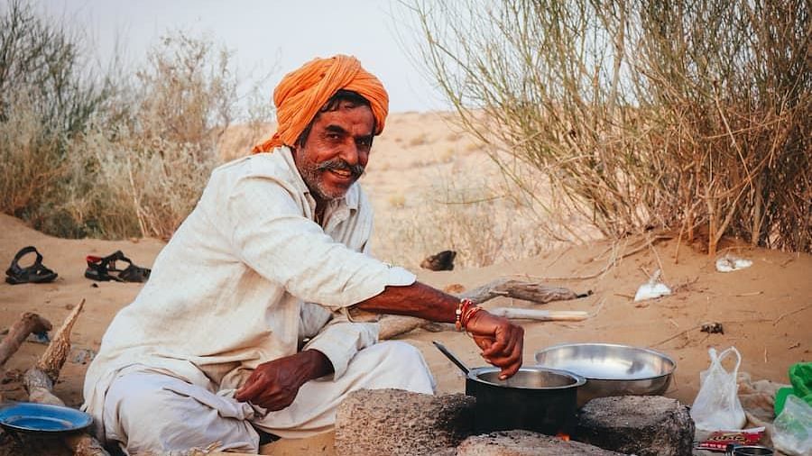 A villager cooking in the desert with shrubs behind him - MANVAR Resort & Desert Camp