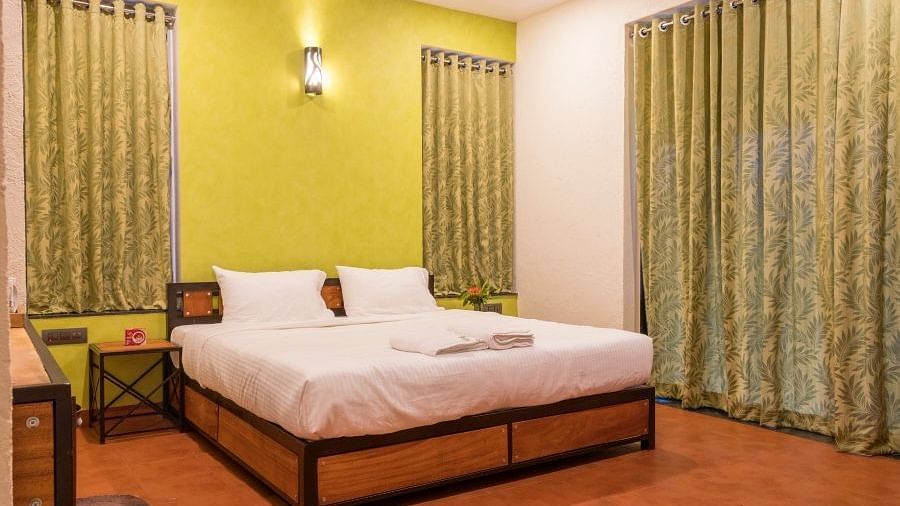 A bedroom with a wooden bed frame, white linens, lime green walls, matching curtains, and a dark wood side table.