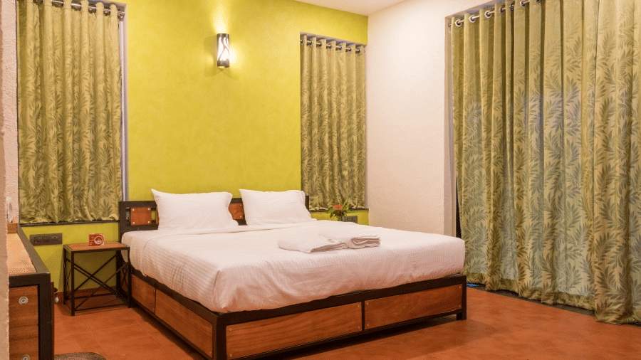 Deluxe Room with a wooden bed frame, white linens against a lime green wall, matching curtains at Forest Escapes, the best resort in Satara