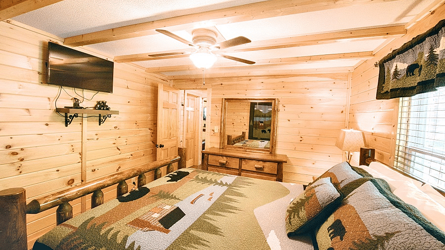 a bedroom featuring a plush double bed with a wall mounted television right opposite to it with a window behind the bed - Historic Tapoco Lodge