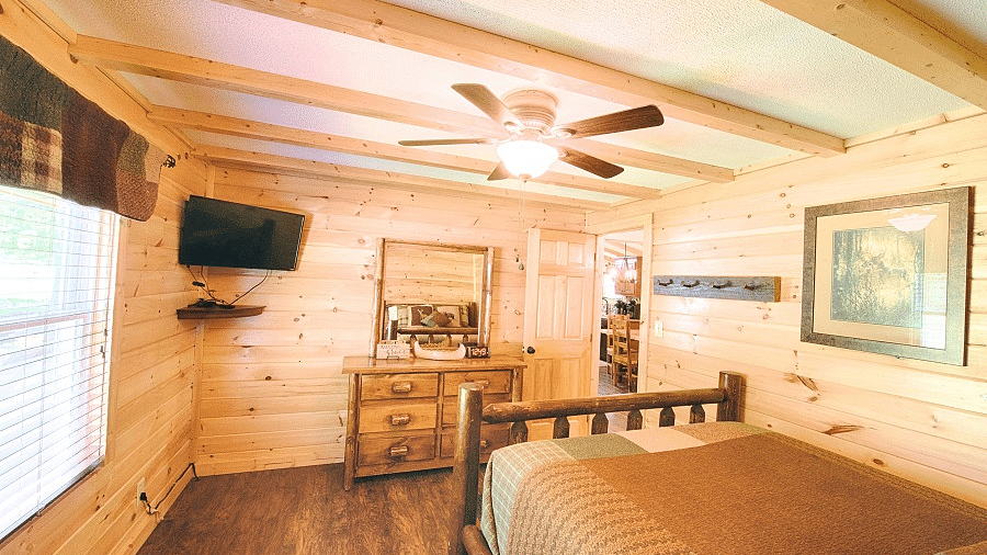 a cozy room with wooden walls and flooring featuring a double bed and wall mounted television - Historic Tapoco Lodge