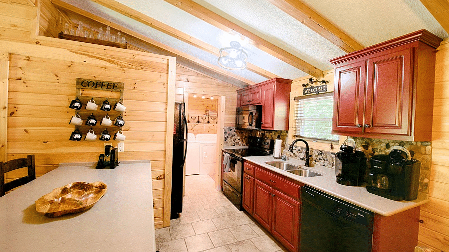 a fully equipped kitchen with red and black colored cabinets and modern appliances kept over a white counter top - Historic Tapoco Lodge