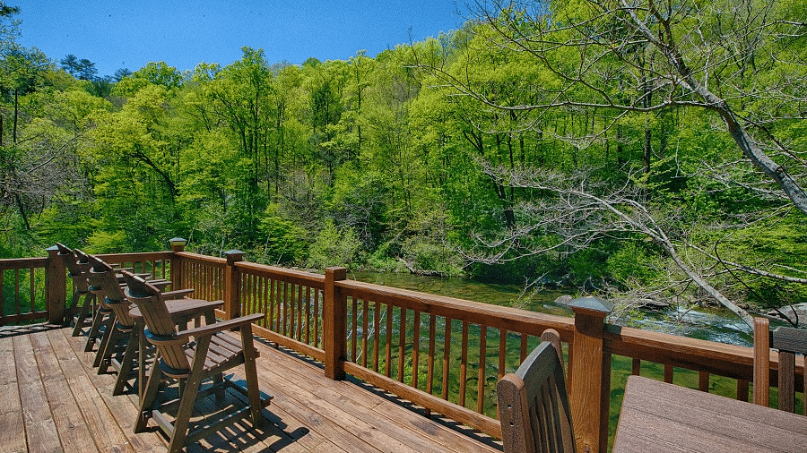 a wooden porch protected by hand railings with several wooden chairs lined up facing towards the forest - Historic Tapoco Lodge