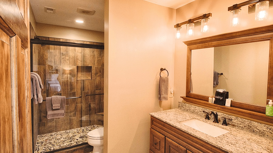 a bathroom with brown tiles featuring a washbasin with a wide wood framed mirror and a shower area - Historic Tapoco Lodge