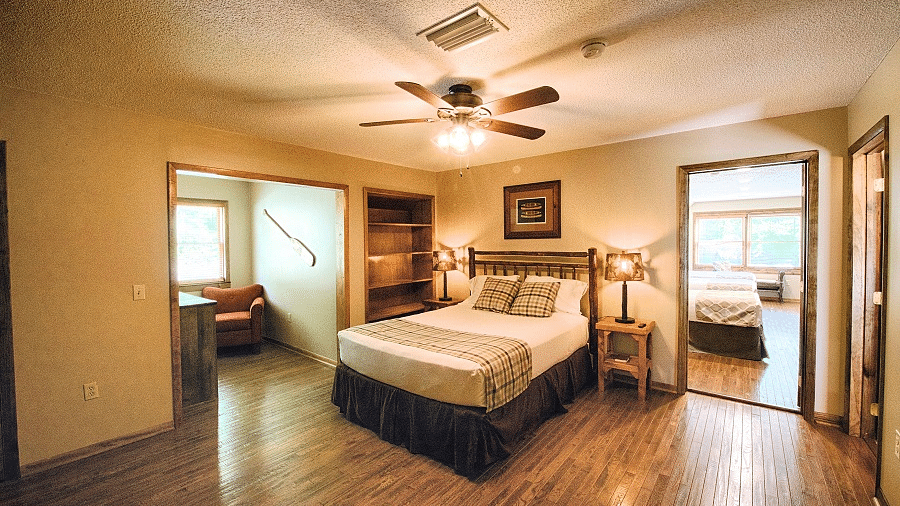 a room with wooden flooring featuring a cozy double bed with a ceiling fan right above it - Historic Tapoco Lodge