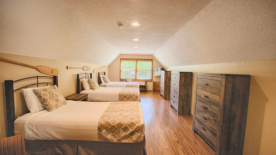 a room with a three single beds each facing towards a wooden storage drawer along with a window in the far end of the room - Historic Tapoco Lodge