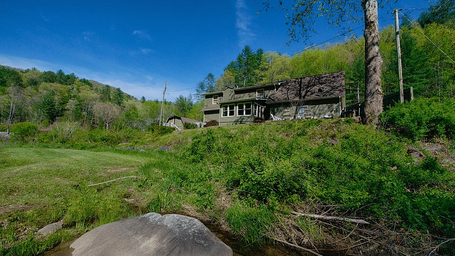 exterior image of the river house overlooking a lush green estate with a clear blue sky in the background - Historic Tapoco Lodge
