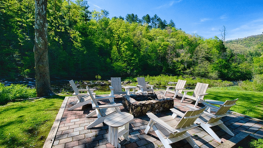 an outdoor seating area with a fire pit in the middle surrounded by wooden chairs amidst lush greenery - Historic Tapoco Lodge