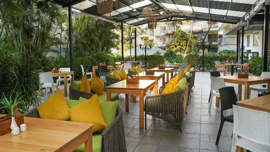 An open-air dining seating with wooden chairs around tables in Aqua Vida Restaurant at Indie Stays Resort, Goa.