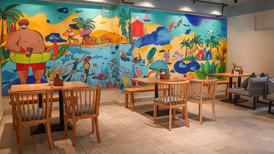 Dining seating with wooden chairs around tables with colorful background in Aqua Vida Restaurant at Indie Stays Resort, Goa.